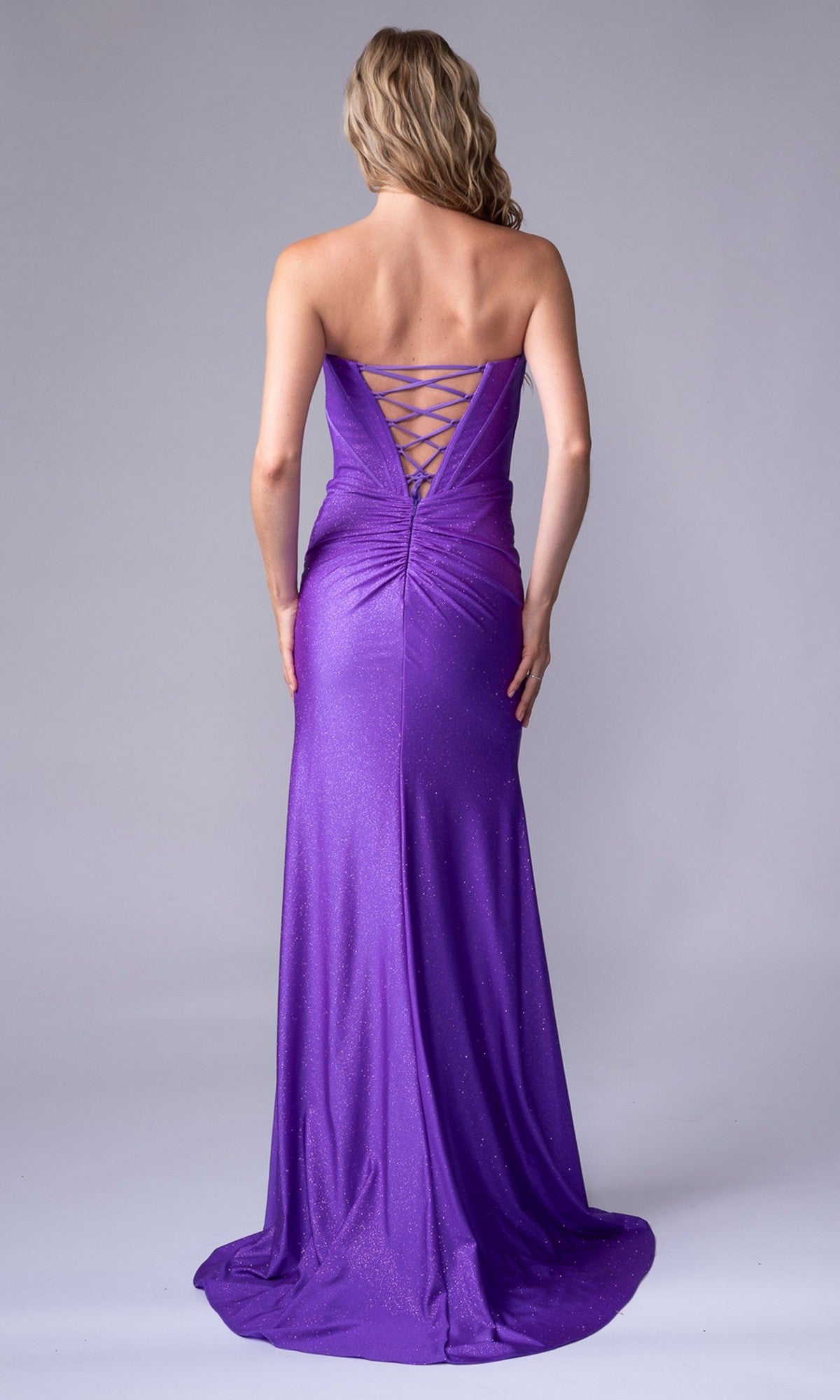 A woman faces away in the Nina Canacci 1608, a floor-length strapless purple gown with a lace-up back and slight shimmer—ideal as a form-fitting special occasion dress.